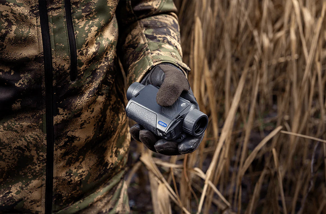 Person in camouflage holding a rangefinder in a natural setting