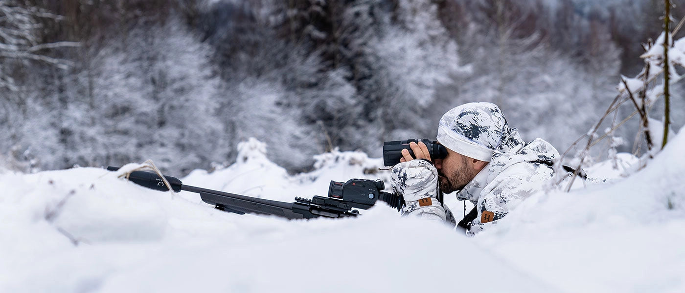 Person in camouflage gear with a rifle in a snowy forest